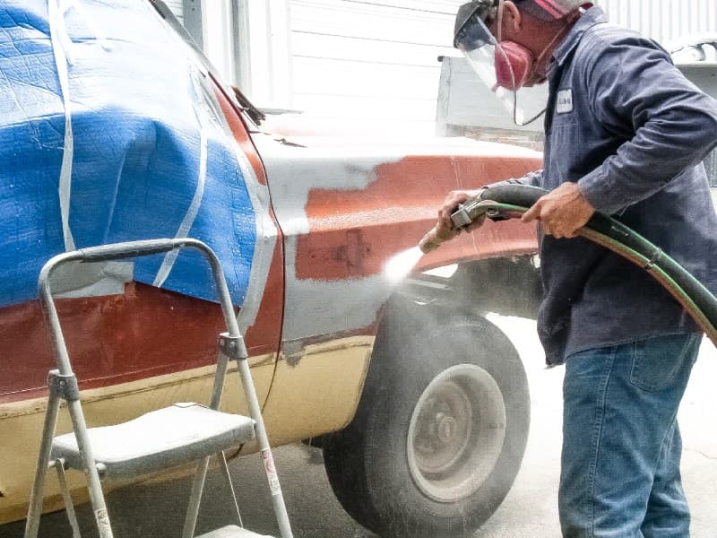 Technician stripping paint from a vehicle body with abrasive blasting
